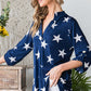 Woman wearing Heimish Full Size Roll-Tab Sleeve Star Print Top with white stars, styled for casual chic look with adjustable sleeve length.