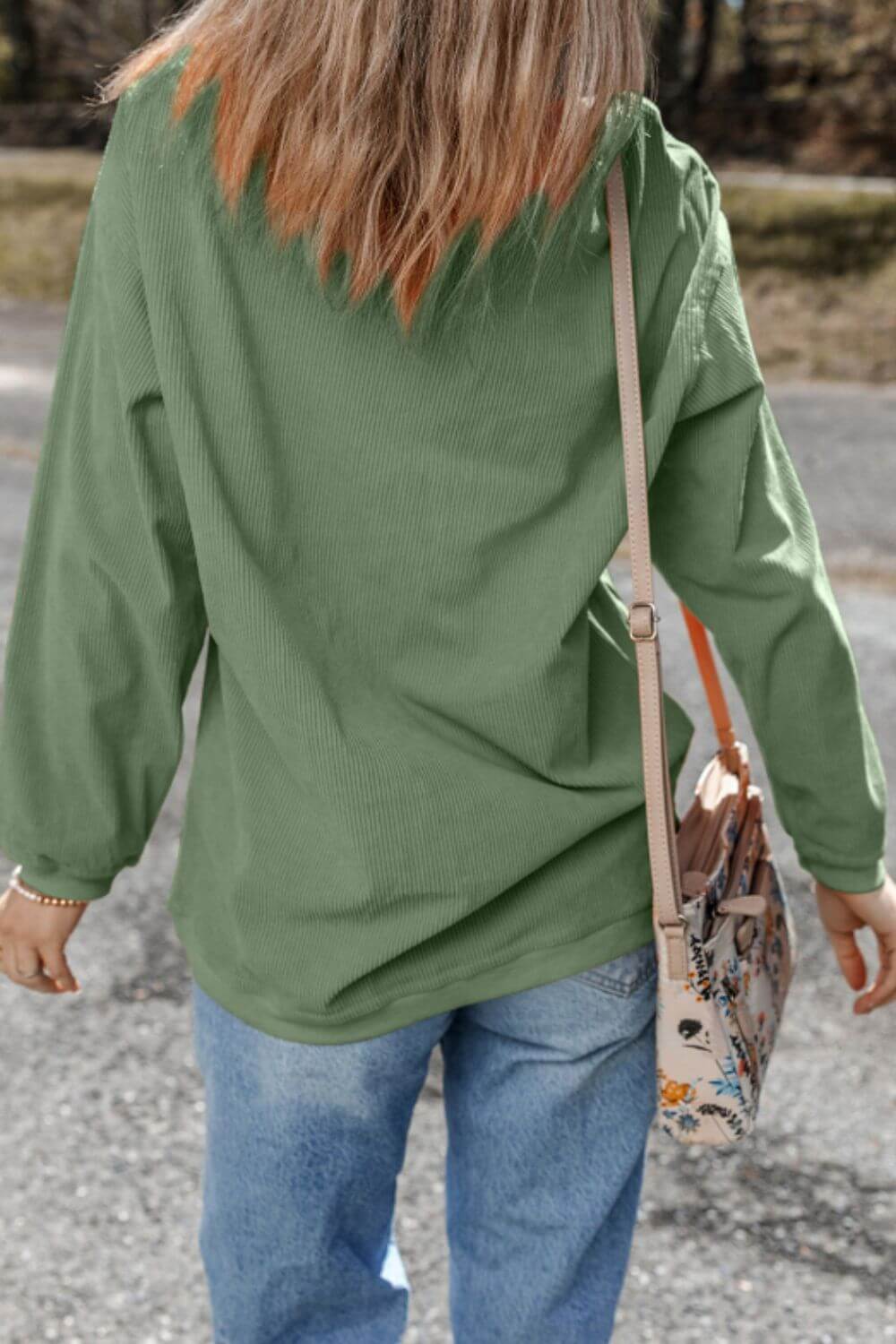 Woman viewing from behind in a green long sleeve top, paired with casual jeans and a floral crossbody bag.