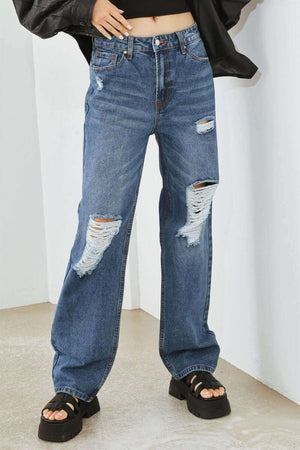 Distressed high waist jeans with rips and fraying, paired with a black top and sandals for a trendy, casual look