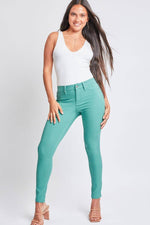 Model wearing YMI Jeans Hyperstretch Mid-Rise Skinny Pants in green paired with a white tank top, showcasing a sleek and versatile look.