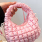 Pink quilted puffy crossbody bag with removable strap and unique design, perfect for fashion-forward versatility.