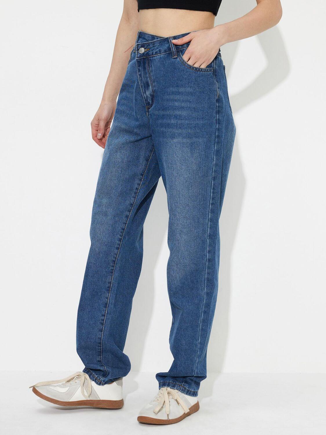 Woman wearing asymmetric waist jeans with pockets, buttoned design, made of 85% cotton and 15% polyester, paired with white sneakers.