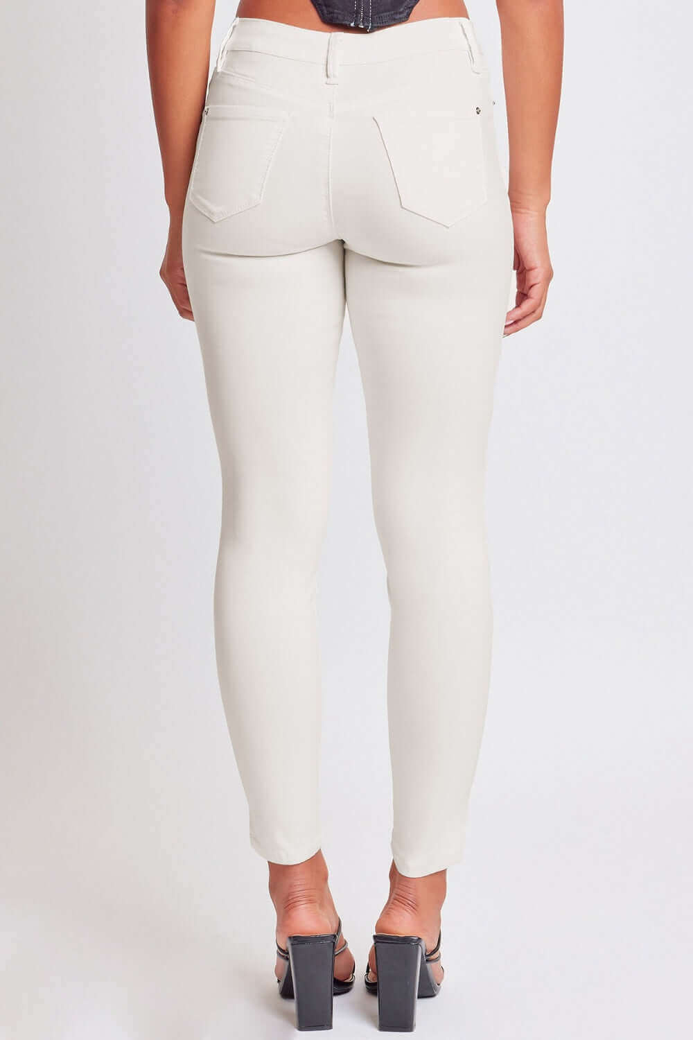 Woman wearing YMI Jeans Hyperstretch Mid-Rise Skinny Jeans in white, showcasing back view and stylish fit.