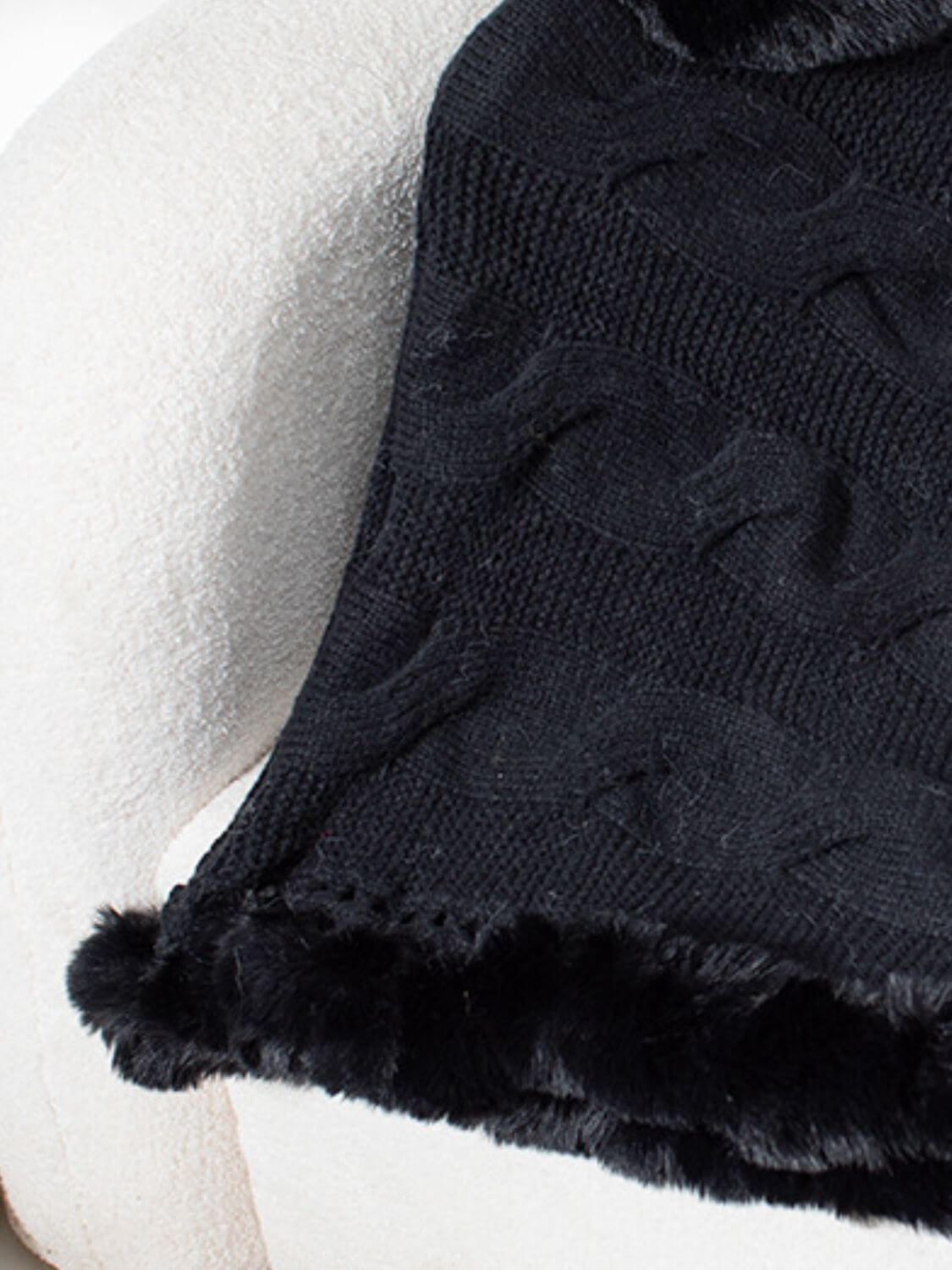 Black Bella Road Fuzzy Hem Cable-Knit Poncho draped on a plush chair, showcasing its cozy texture and stylish design.