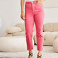 Woman wearing Crop Dylan Full Size Tummy Control High Waist Raw Hem Jeans in pink with black heels in stylish living room. RFM Jeans.