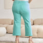 Woman wearing Crop Chloe Full Size Tummy Control High Waist Raw Hem Jeans in mint color, showing back view in a living room.