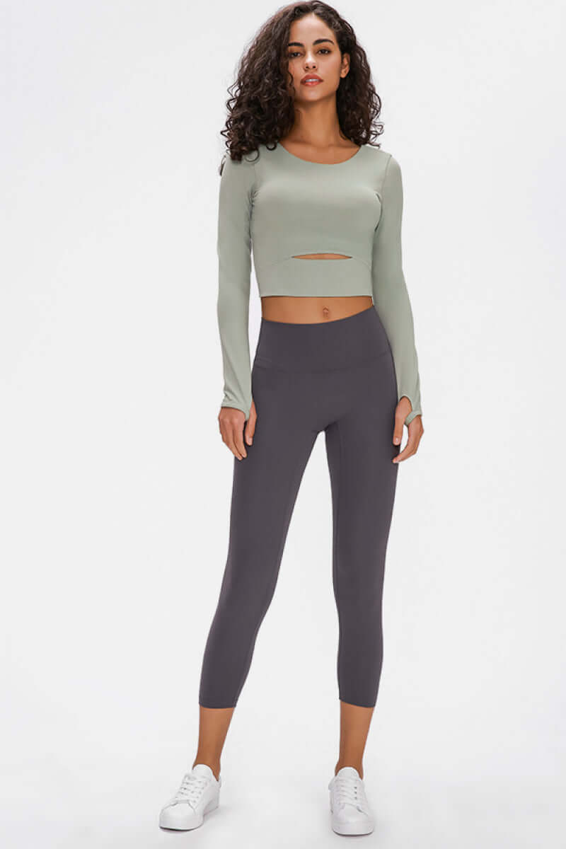 Model showcasing the Millennia Long Sleeve Cropped Top in green paired with gray leggings, perfect for stylish workouts.