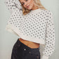 Trendy woman in patterned round neck sweater and black jeans, striking a relaxed pose for a chic and cozy fashion look.