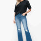 Model showcasing bytos Full Size Raw Hem Distressed Bootcut Jeans with black top and nude heels, flaunting trendy style.