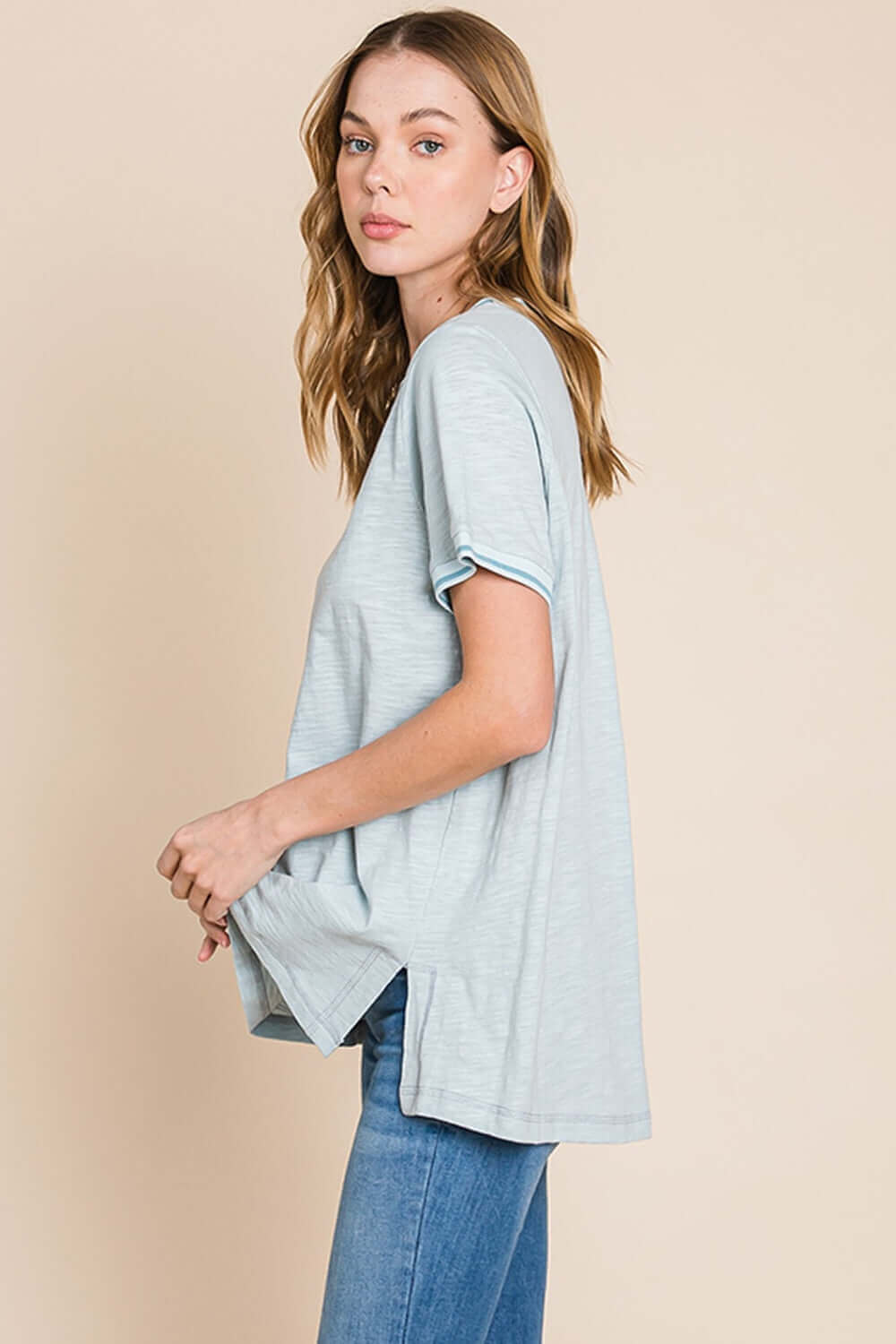 Woman wearing a contrast trim short sleeve slit T-shirt in light grey, paired with blue jeans, showcasing side slit and relaxed fit.