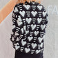 Woman wearing Bella Heart Sweater with black and white heart contrast design, dropped shoulder, and slightly stretchy fabric.