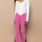 Stylish model wearing pink raw hem embroidered flare pants with a white top and trendy blue sandals.