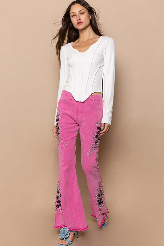 Stylish model wearing pink raw hem embroidered flare pants with a white top and trendy blue sandals.