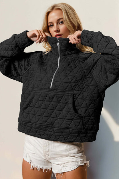 Woman modeling black quilted half zip sweatshirt with pocket, showcasing cozy and stylish design.