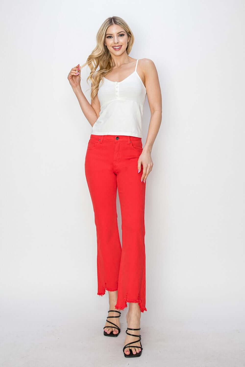 Woman wearing red Raw Hem Bootcut Jeans with Pockets by Risen Jeans, paired with a white sleeveless top and black strappy sandals.