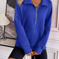 Woman wearing Ivy Lane Half Zip Raglan Sleeve Sweatshirt in royal blue, standing indoors with hands crossed, paired with black shorts.