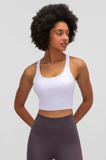 Stylish woman wearing a white Millennia Racerback Sports Bra, ready for yoga, showcasing comfort and sporty design.