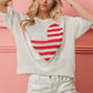 Woman wearing striped heart contrast knit top with distressed white shorts in front of a pink wall