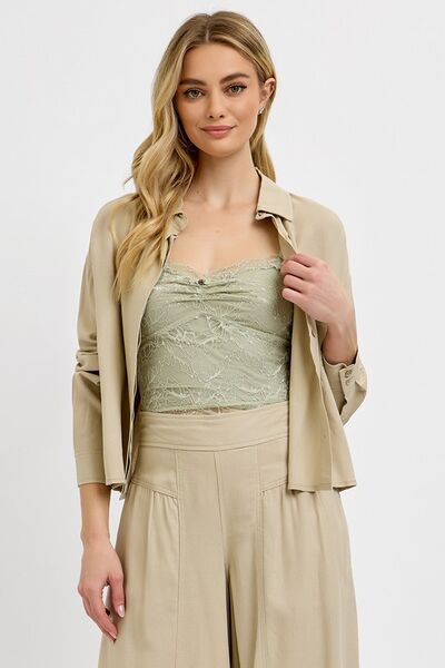 Stylish woman in a beige button-down shirt and light green tank top, showcasing a chic, casual look.