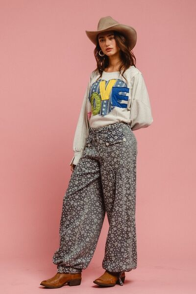 Model in a stylish LOVE sweatshirt and floral pants, showcasing a charming and cozy outfit with hat and boots.