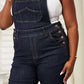 Woman wearing high waist classic denim overalls from Judy Blue Jeans, showcasing a flattering silhouette and a straight-leg cut.