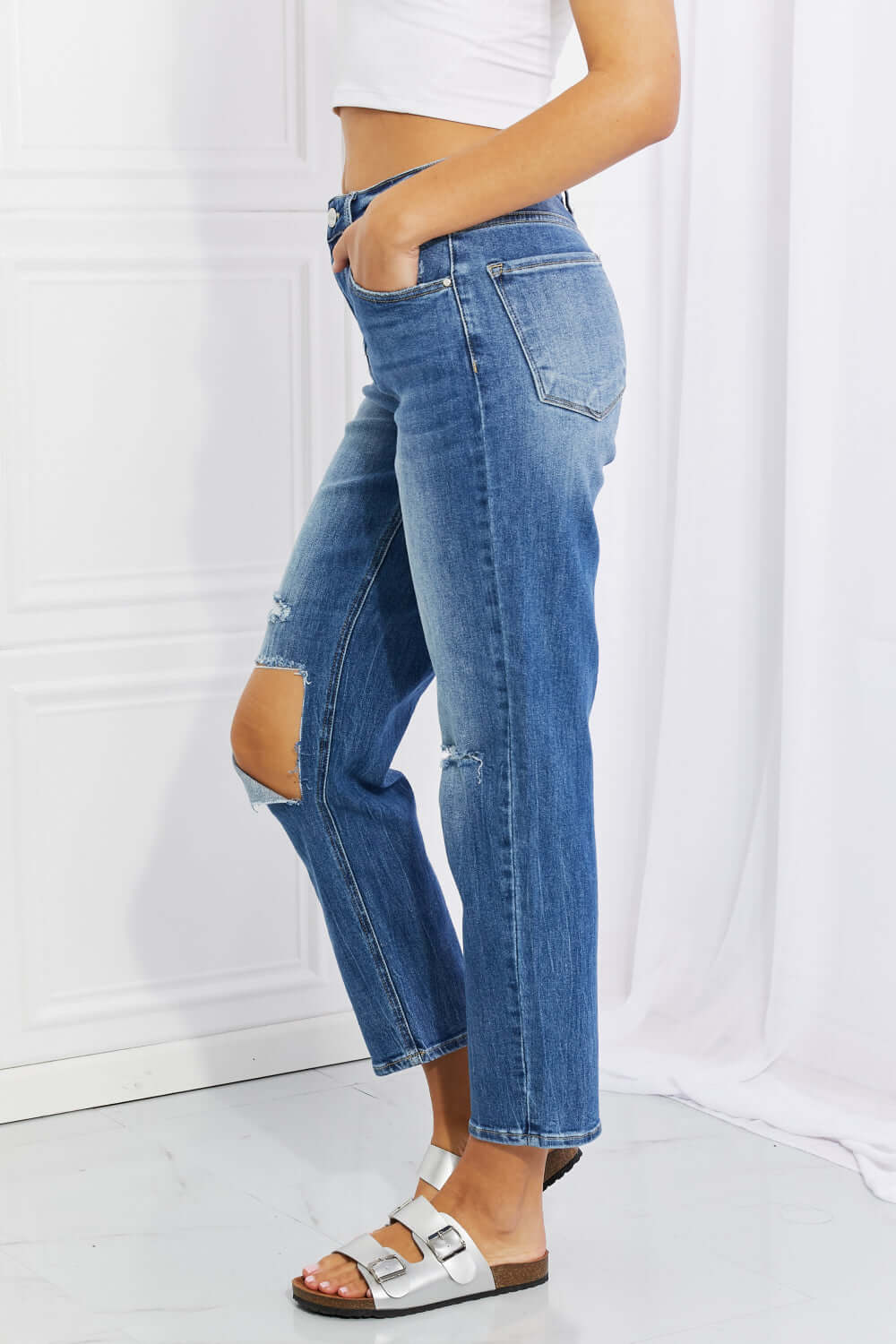 Side view of Emily High Rise Relaxed Jeans with ripped knee detail, casual solid blue Risen Jeans for a timeless and edgy look.