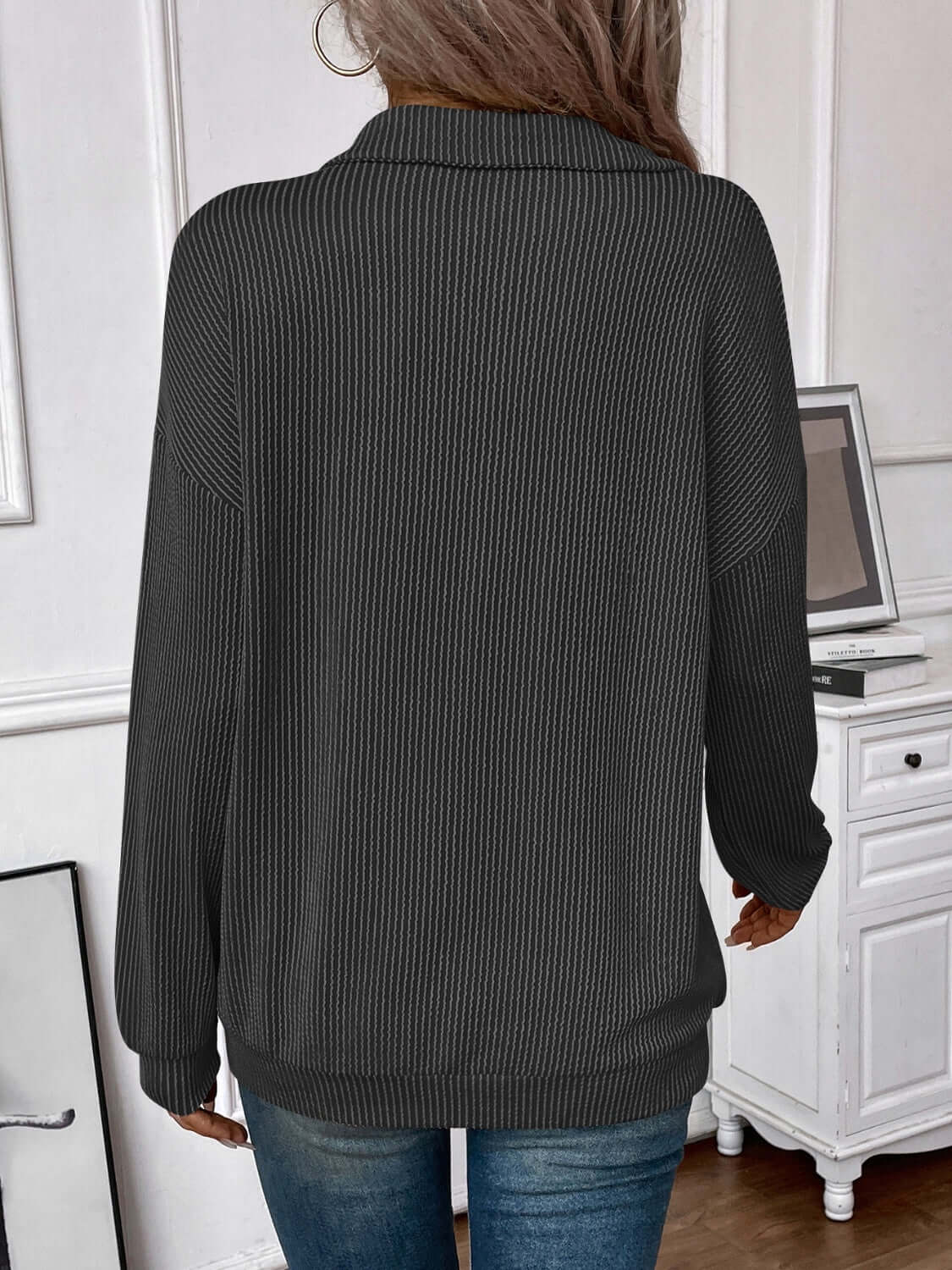 Woman wearing a striped half zip long sleeve T-shirt in a modern home office, showcasing the back view of the garment