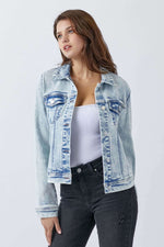 Woman modeling Risen Jeans button-up washed denim jacket with buttoned chest pockets, styled with black jeans and a white top