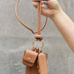 Nicole Lee USA Vegan Leather 3-Piece Lanyard Set with AirPods Case held by a hand against a concrete background