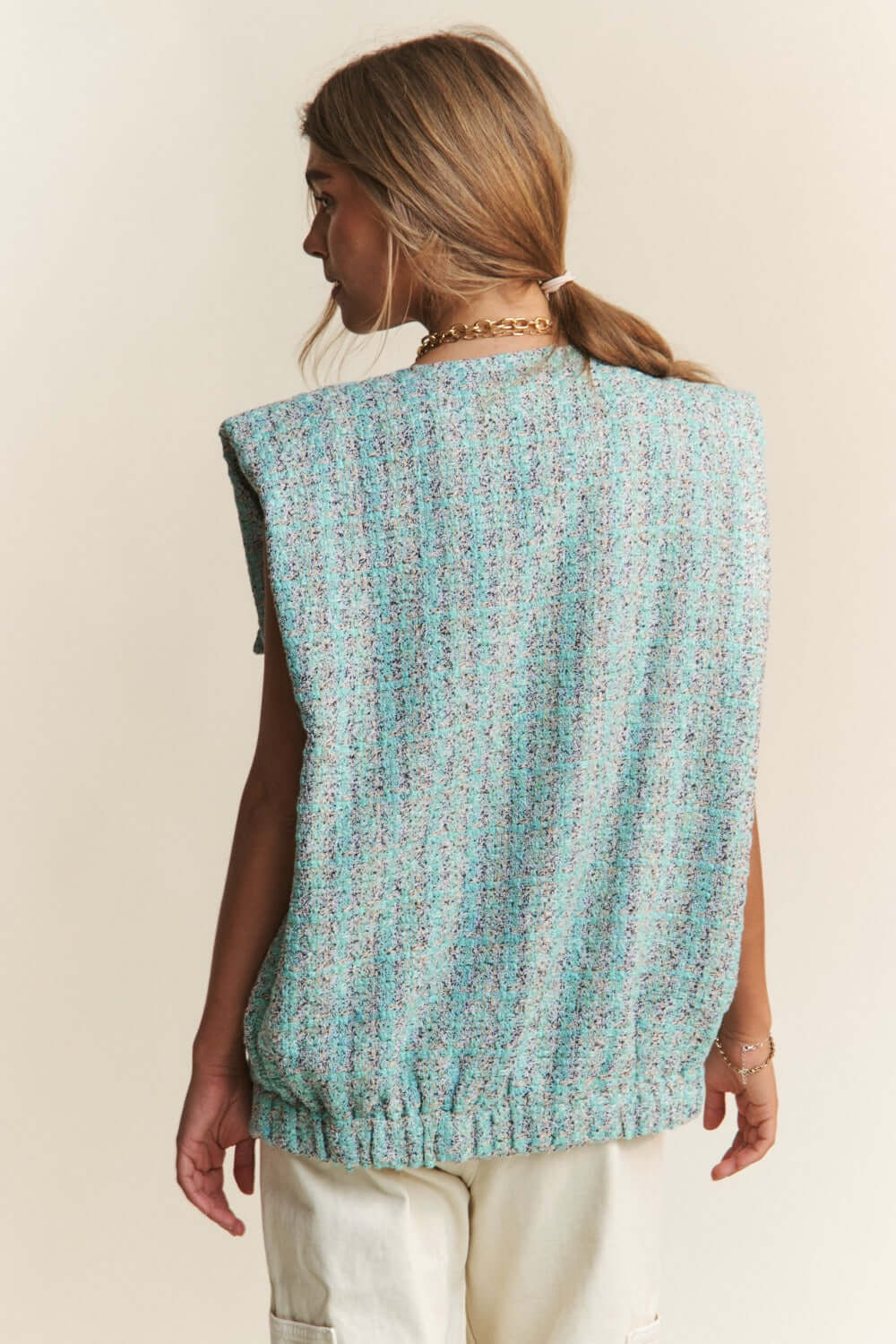 Woman wearing a J.NNA frayed tweed padded shoulder vest in blue, showcasing the stylish back design.