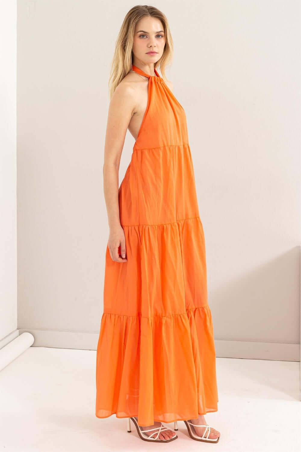 Model wearing an orange halter neck cover up maxi dress with a tiered silhouette and open back design.