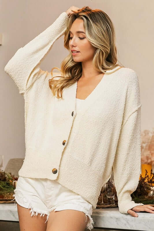 Stylish model wearing a cream V-Neck Button Up Dropped Shoulder Cardigan paired with shorts in a cozy indoor setting.