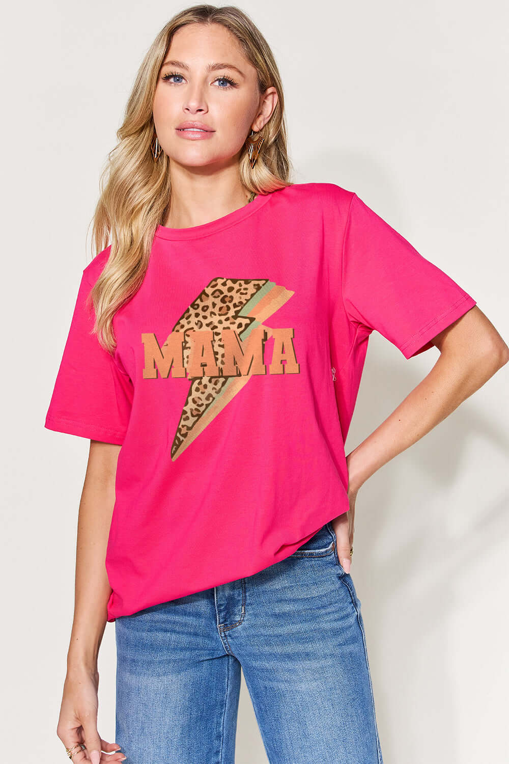 Woman wearing a pink MAMA round neck short sleeve T-shirt with leopard print design, paired with blue jeans.