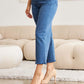 Woman wearing RFM Jeans Crop Chloe Full Size Tummy Control High Waist Raw Hem Jeans with nude heels in a stylish living room.