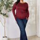 Curvy model wearing a maroon drawstring round neck long sleeve top with jeans, standing next to a plant in a stylish indoor setting.