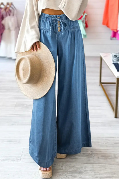 Woman wearing drawstring elastic waist wide leg jeans holding a straw hat in a stylish boutique setting.