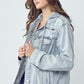 Young woman modeling a RISEN distressed drawstring hooded denim jacket in light wash, perfect for casual outfits.