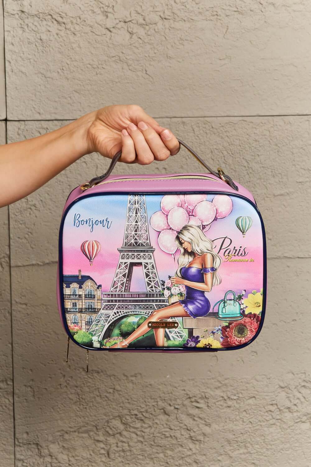 Person holding Nicole Lee USA printed handbag with Parisian design of Eiffel Tower, balloons, and a woman sitting on a bench