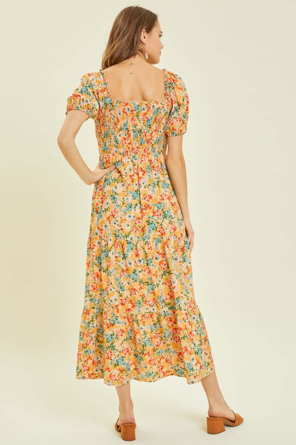 Woman wearing a HEYSON floral smocked tiered midi dress, showcasing the back view and vibrant flower pattern.