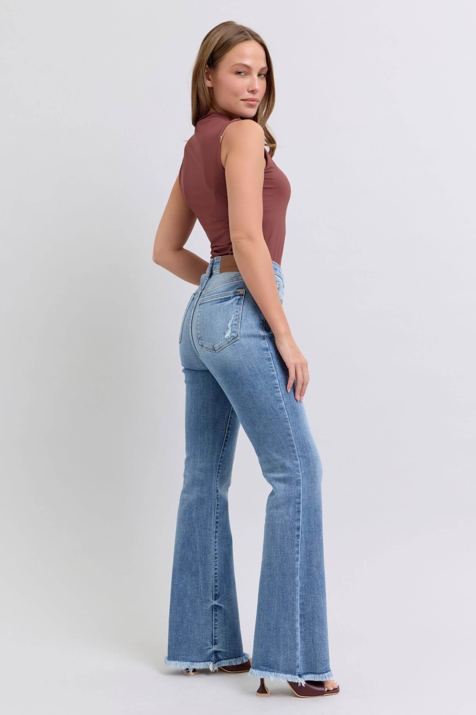 Woman in raw hem high rise bootcut jeans, showcasing a trendy retro style from the back. Perfect for a fashionable look!