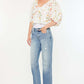 Woman wearing Kancan mid-rise frayed hem straight jeans in medium wash with a floral blouse and white sneakers.