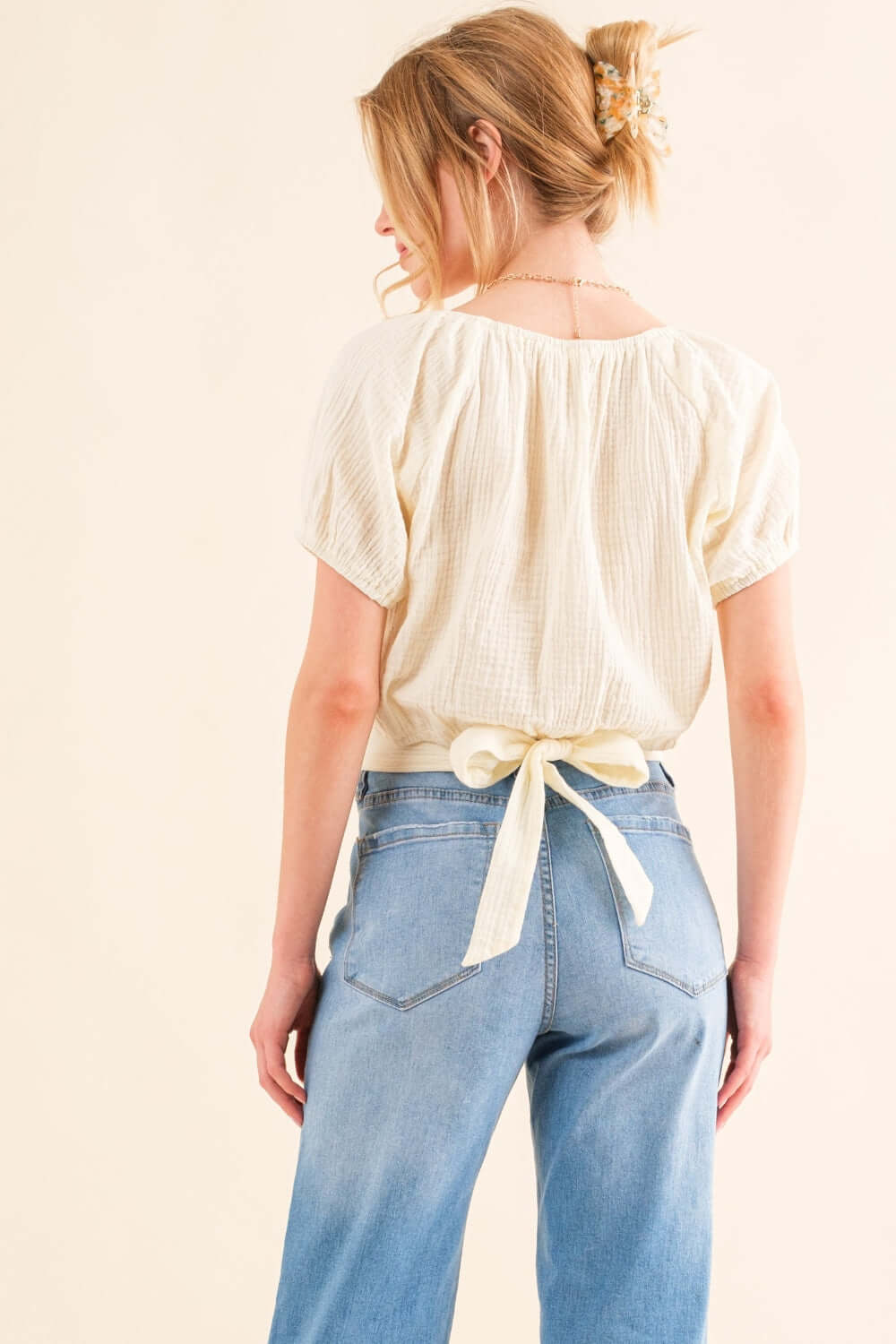 Back view of a stylish Back Waist Tie Cropped Blouse in light fabric, perfect for high-waisted pants or skirts.