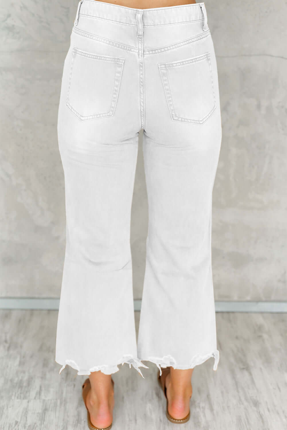 Distressed raw hem white jeans with pockets, back view, showing trendy flared leg design.