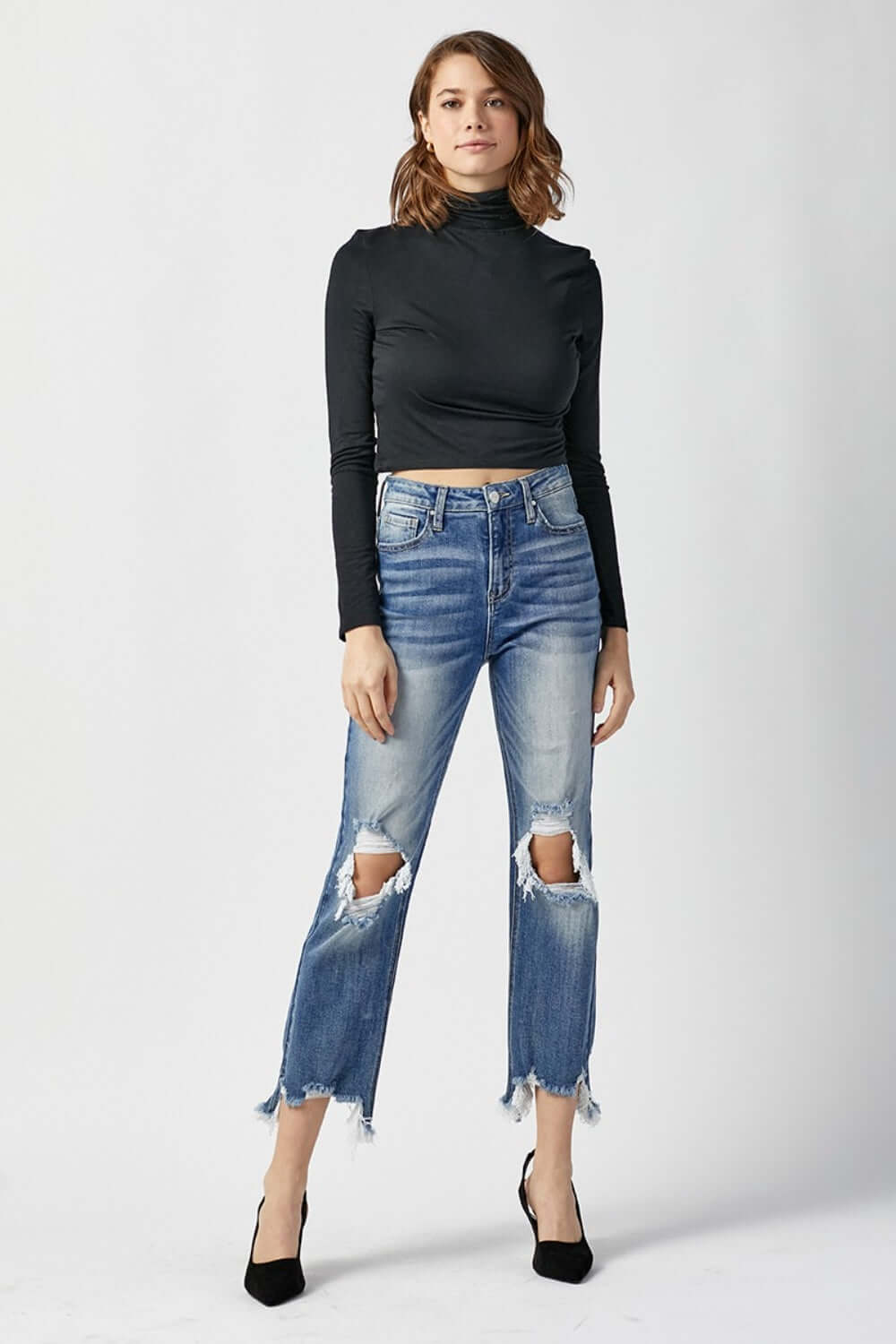 Model wearing High Waist Distressed Frayed Hem Cropped Straight Risen Jeans, black turtleneck, and black heels against a white background