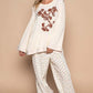 Model wearing a cream embroidered long sleeve knit top with patterned pants, showcasing a relaxed and stylish outfit.