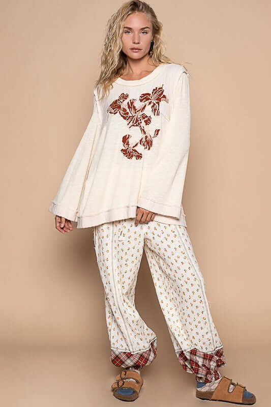 Model wearing a cream embroidered long sleeve knit top with patterned pants, showcasing a relaxed and stylish outfit.