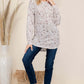 Woman in leopard print long sleeve blouse and jeans, posing stylishly against a neutral backdrop with natural decor.