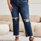 Woman wearing RFM Jeans Crop Dylan full size tummy control distressed high waist raw hem jeans, standing in stylish living room.