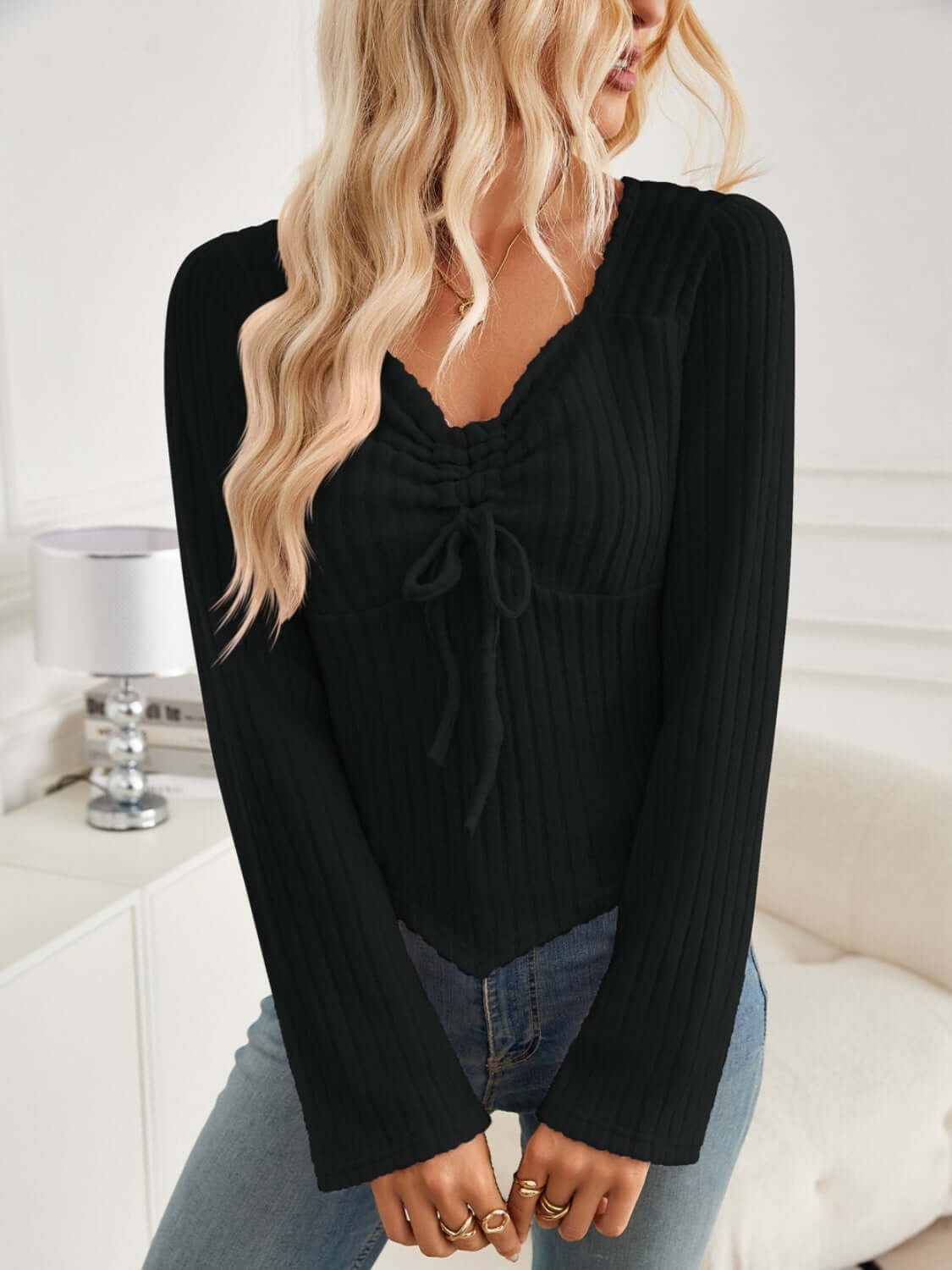 Woman wearing Bella Road ribbed drawstring long sleeve black T-shirt with jeans in a cozy room.