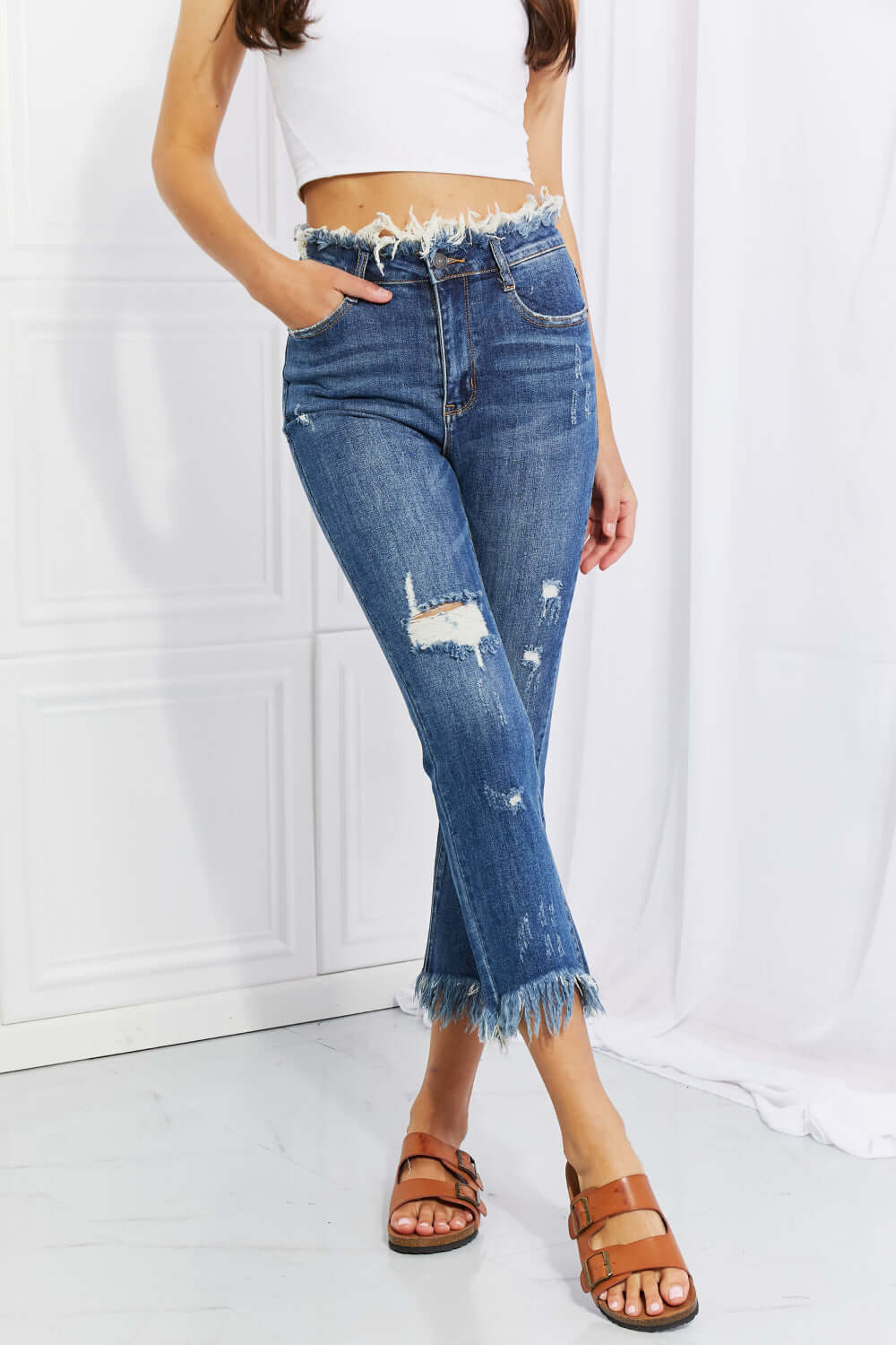 Woman wearing Undone Chic Straight Leg Jeans with distressed details and raw hem, paired with a crop top. Casual Risen Jeans style.